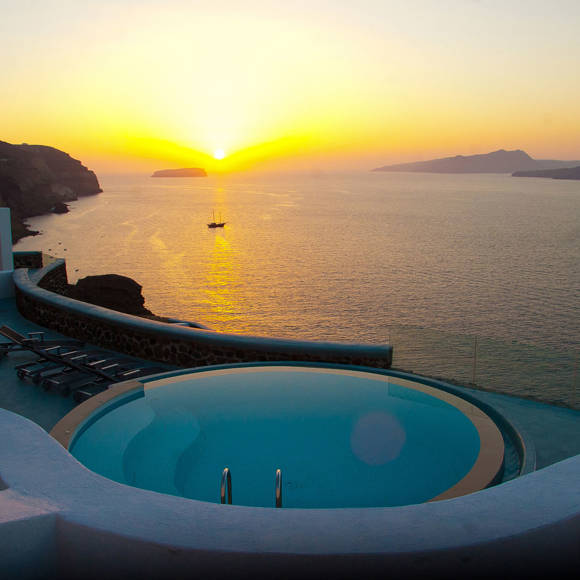 Sunset view over a round infinity pool and lounge chairs at Grand Ambassador hotel, perched on a cliff overlooking the sea