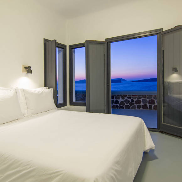 Grand Ambassador Santorini Villa master bedroom with double bed, terrace access, and sea view at dusk