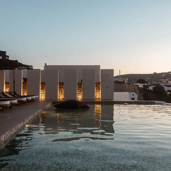 Grand Ambassador pool bar at sunset with mosaic pool, cushioned sunbeds, and illuminated privacy walls