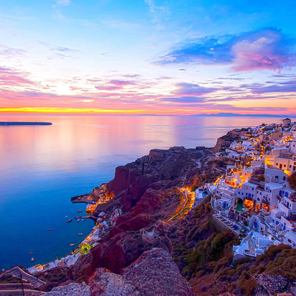 Santorini clifftop village glowing at sunset with colorful sky and sea views