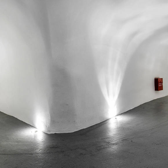 Curved, white-walled tunnel in Grand Ambassador with smooth concrete floor and recessed lights along the base, leading to two separate paths