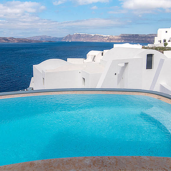 Infinity pool with ocean view at Grand Ambassador hotel featuring white architecture and clear blue sky