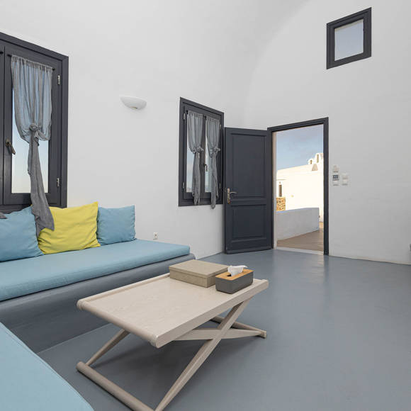 Grand Ambassador Santorini Serenity Two Bedroom Suite living area with built-in blue sofa, yellow accent pillow, and minimalist decor