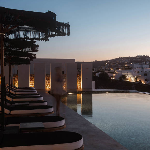 Grand Ambassador pool bar evening scene with pool, sunbeds, parasols, and illuminated hillside village