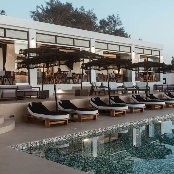 Grand Ambassador pool bar evening view with mosaic pool, cushioned sunbeds, black parasols, and open restaurant