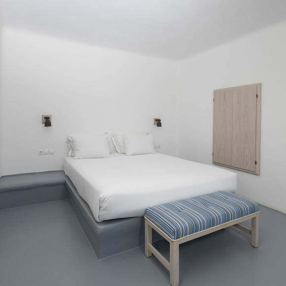 Grand Ambassador Santorini Serenity Two Bedroom Suite guest bedroom with double bed, striped bench, and minimalist Cycladic decor