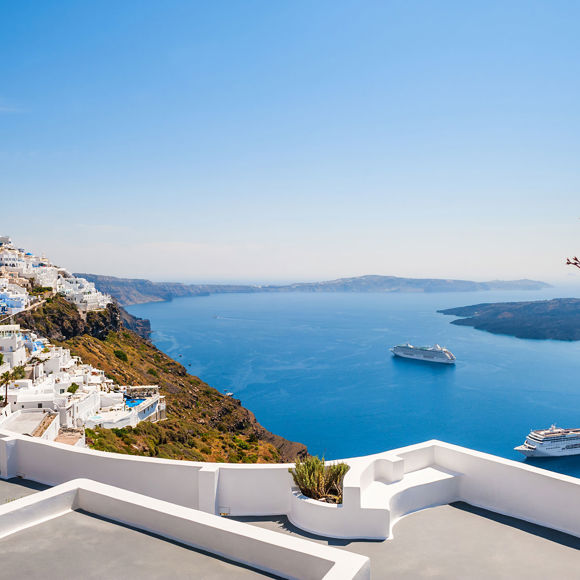 Santorini cliffside village with whitewashed buildings, cruise ships in the caldera, and bright blue sky