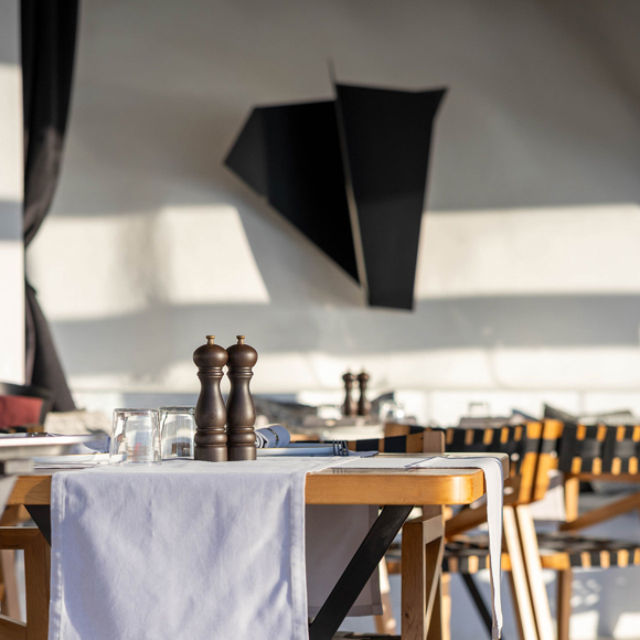 Grand Ambassador Dione restaurant table with pepper mills, glassware, and modern wall decor