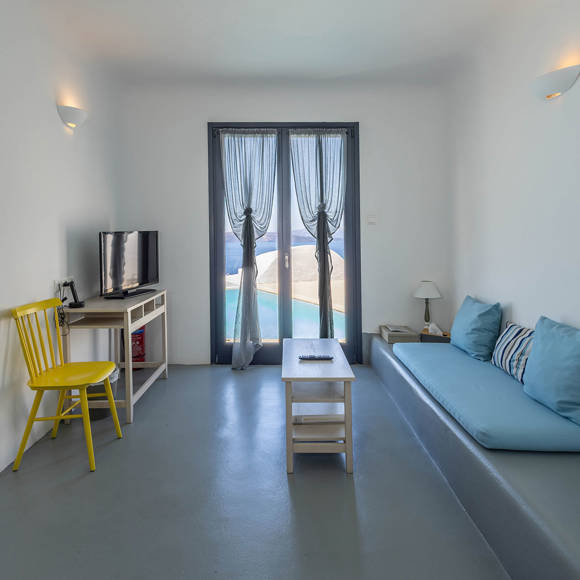 Grand Ambassador Santorini Petit Suite cozy living area with built-in blue sofa, work desk, and terrace access