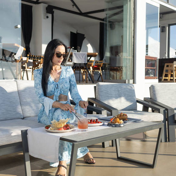 Woman dining on outdoor sofa at Grand Ambassador hotel with plates of food and cocktail on table