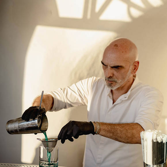 Grand Ambassador pool bar bartender pouring blue cocktail into a glass through a strainer at sunset