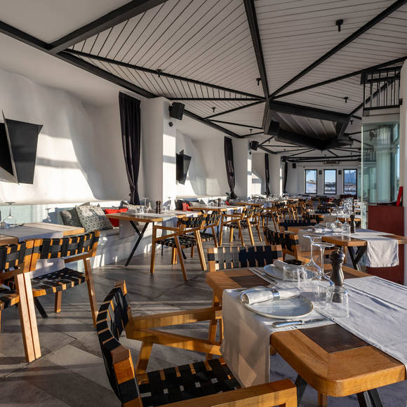 Grand Ambassador Dione restaurant spacious dining area with modern wooden chairs, set tables, and large glass windows