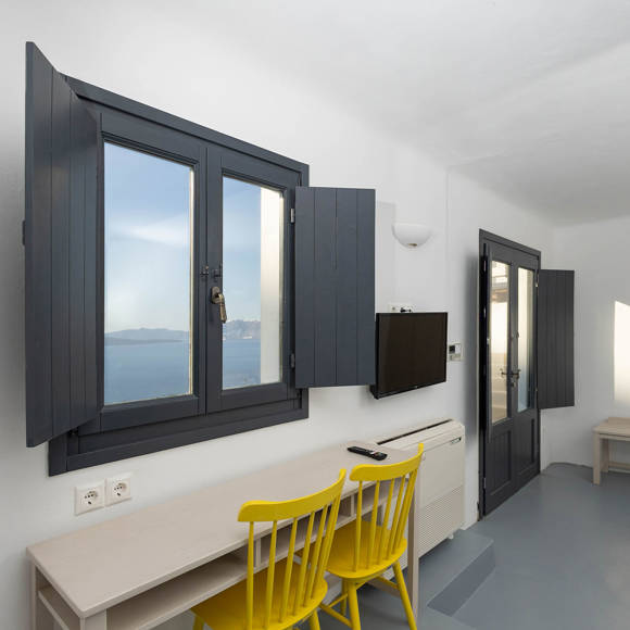 Grand Ambassador Santorini Serenity Two Bedroom Suite work desk with yellow chairs, window and balcony views of the caldera