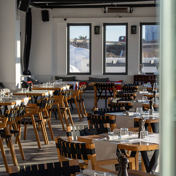 Grand Ambassador Dione restaurant indoor dining room with wooden chairs, set tables, and large windows