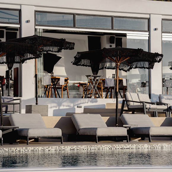 Grand Ambassador Dione restaurant poolside lounge area with sunbeds, umbrellas, and glass facade