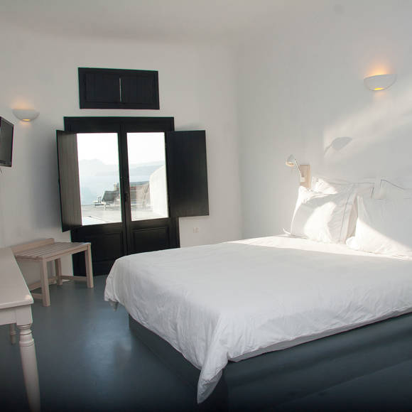 Grand Ambassador Santorini Superior Deluxe Room bright bedroom with double bed, built-in desk, and panoramic caldera view
