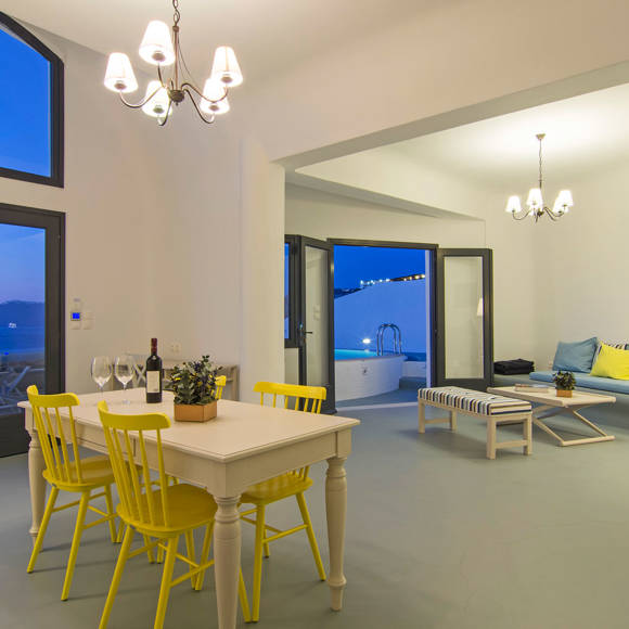 Grand Ambassador Santorini Villa dining area with yellow chairs, chandelier lighting, and caldera sea view