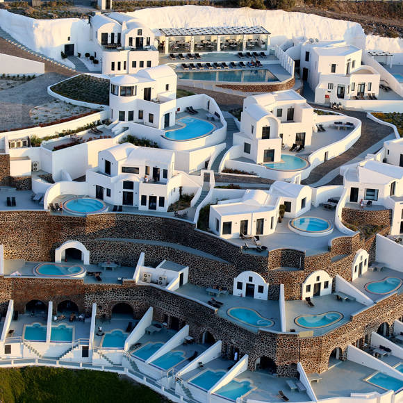 Cliffside resort with multiple white buildings, each featuring private pools and terraces, built on terraced levels with stone walls