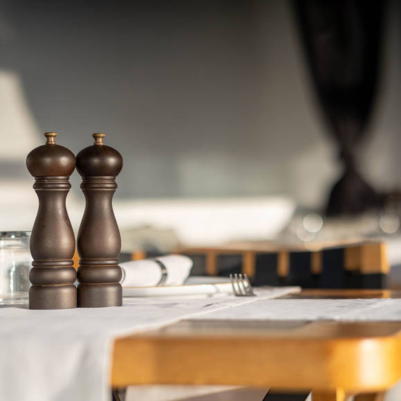 Grand Ambassador Dione restaurant table close-up with wooden pepper mills and glassware in sunlit dining area