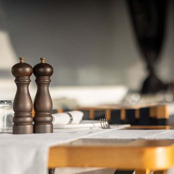 Grand Ambassador Dione restaurant table close-up with wooden pepper mills and glassware in sunlit dining area
