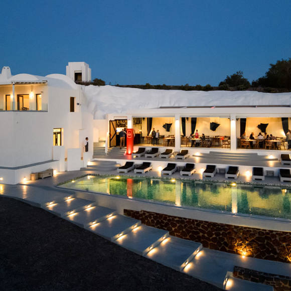 Grand Ambassador swimming pool illuminated at night with modern sunbeds and poolside restaurant in Santorini