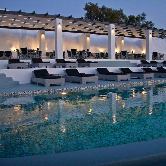 Grand Ambassador swimming pool lounge area at dusk with modern sunbeds, illuminated pergola, and poolside bar