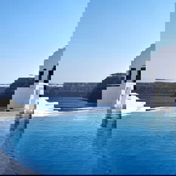 Infinity pool overlooking the sea and volcanic cliffs at Grand Ambassador hotel, with whitewashed buildings under a clear blue sky