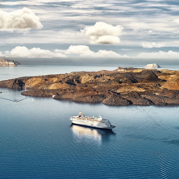 Santorini volcanic island with cruise ship in calm blue waters under partly cloudy sky