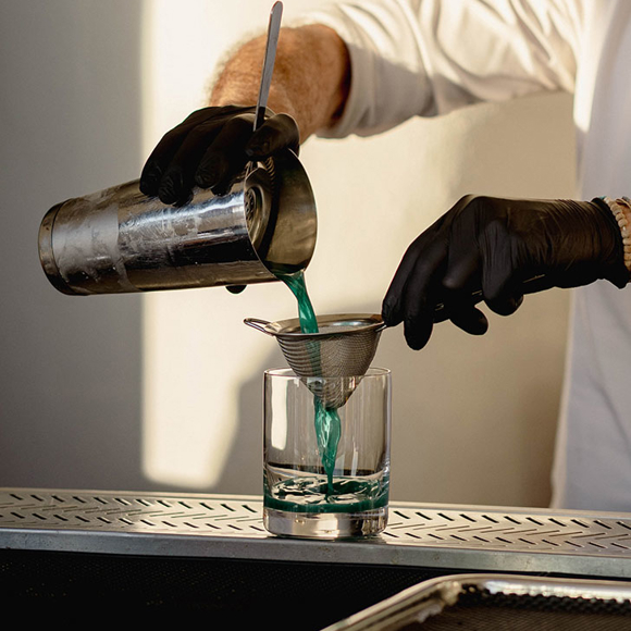 Grand Ambassador pool bar bartender straining and pouring blue cocktail into glass