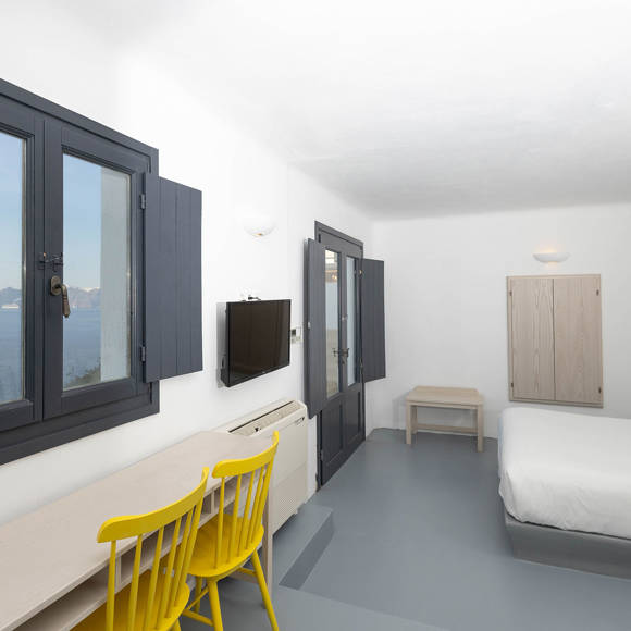 Grand Ambassador Santorini Serenity Two Bedroom Suite bright bedroom with caldera view, desk, yellow chairs, and minimalist Cycladic design