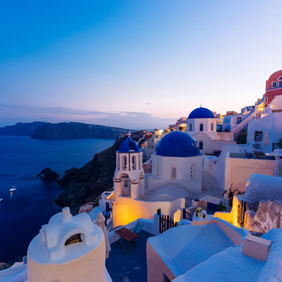 Santorini view of blue-domed churches, whitewashed houses, and caldera at sunset