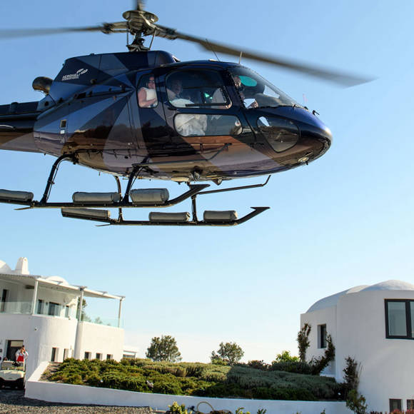 Blue helicopter landing at Grand Ambassador hotel with white buildings and staff guiding
