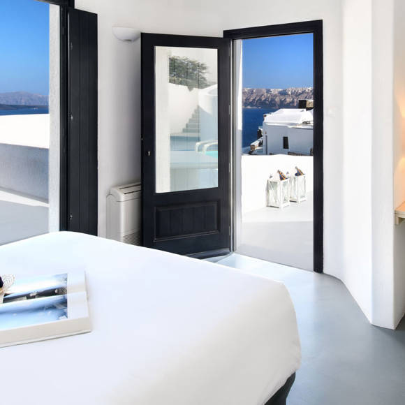 Grand Ambassador Santorini Luxury Suite bright bedroom with sea view and yellow accent chair